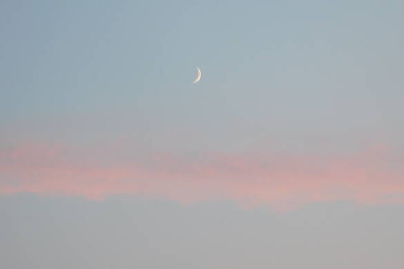 Eine dünne Mondsichel leuchtet am blaugrauen Himmel, der von einer rosaroten Wolke untermalt wird.