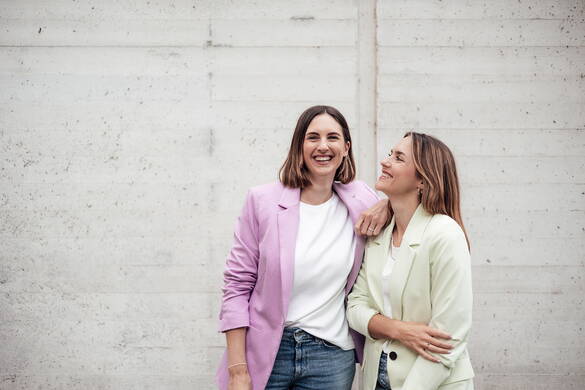 Fabienne Muri und Chantal Muri stehen vor einer Betonwand. Chantal schaut Fabienne an, Fabienne lacht in die Kamera.