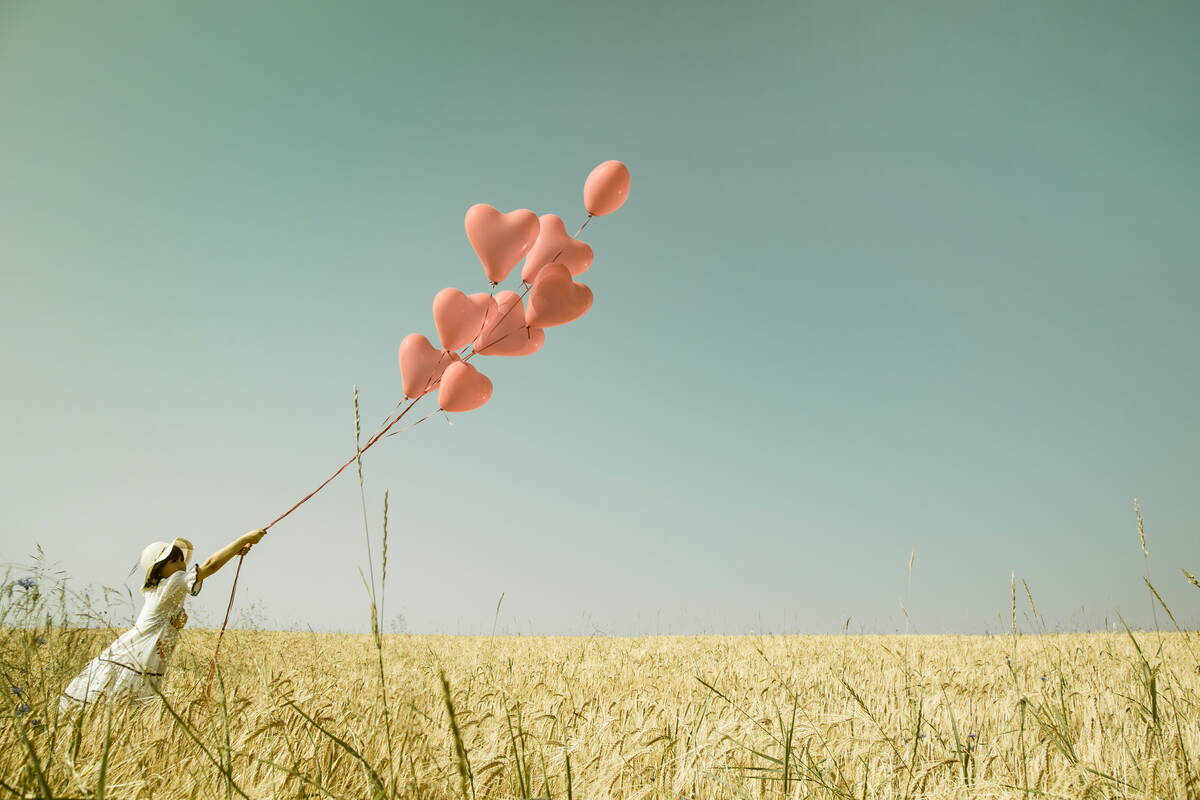 Mädchen auf Feld mit fliegenden Ballonen in der Hand.