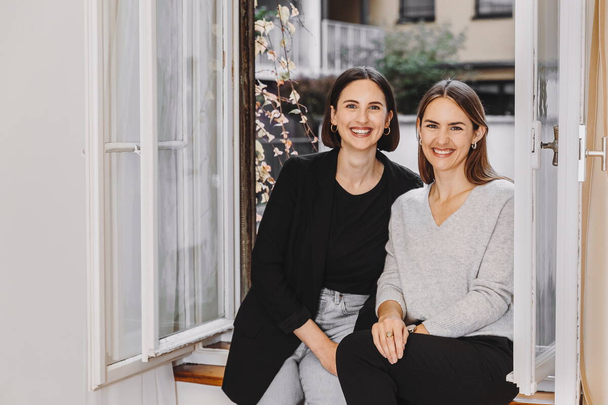 Fabienne Muri und Chantal Muri sitzen gemeinsam bei geöffnetem Fenster auf dem Fenstersims ihrer Coachingspraxis. 